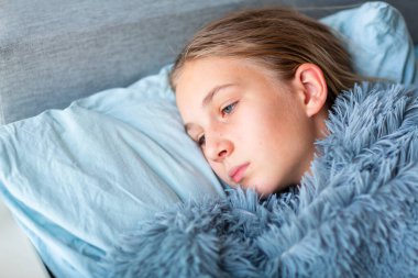 Hasta, yüksek ateşi ve baş ağrısı olan küçük bir kız çocuğu yatakta yatıyor. Eğer hasta hissediyorsan Corona virüsü salgını sırasında evde kal.