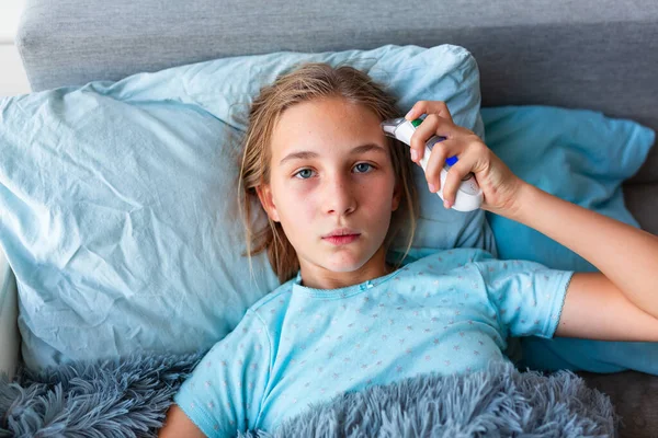 高熱と頭痛のベッドの中で彼女の温度を確認敷設と病気の十代の少女 コロナウイルスの流行時に家にいて病気になったら — ストック写真