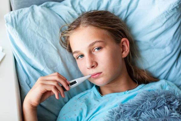 高烧头疼的生病少女躺在床上 嘴里衔着温度计 如果你觉得不舒服 在日冕病毒流行期间呆在家里 — 图库照片