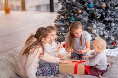 Mutlu çocuklar Noel ağacının yanında eğleniyor ve hediyeler açıyor..