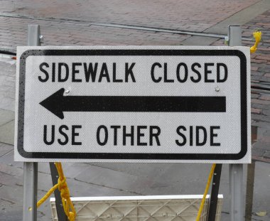 Düzenleyici yol işareti insanları başka bir yol kullanmaları için uyarıyor. Dikdörtgen beyaz ve siyah metal tabela, kaldırım kapalı, diğer tarafı kullan.
