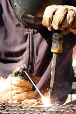 Standart koruma ekipmanı takan bir metal parçasını kaynaklıyor.