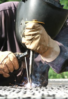 Standart koruma ekipmanı takan bir metal parçasını kaynaklıyor.