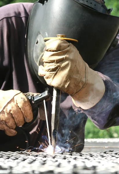 Standart koruma ekipmanı takan bir metal parçasını kaynaklıyor.