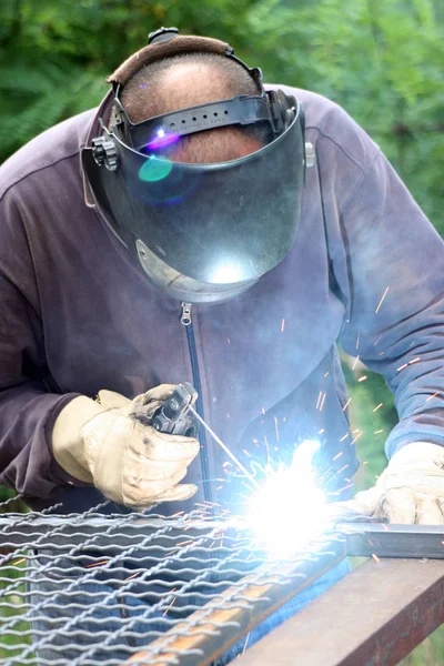 Standart koruma ekipmanı takan bir metal parçasını kaynaklıyor.