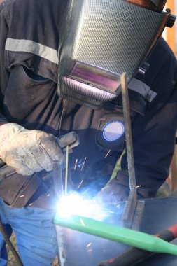 Standart koruma ekipmanı takan bir metal parçasını kaynaklıyor.