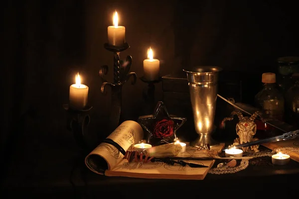 Black Magic Spells. Wiccan spells and herbs. Still Live: Old oil lamps, antique books, dried rose buds, a burning candle in a copper bowl, medicine bottles, lavender, Pulsatilla pratensis on an antique background. Wicca background.