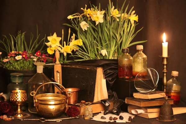 Black Magic Spells. Wiccan spells and herbs. Still Live: Old oil lamps, antique books, dried rose buds, a burning candle in a copper bowl, medicine bottles, lavender, Pulsatilla pratensis on an antique background. Wicca background.