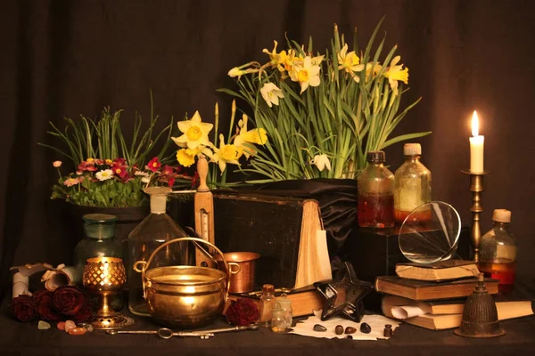 Black Magic Spells. Wiccan spells and herbs. Still Live: Old oil lamps, antique books, dried rose buds, a burning candle in a copper bowl, medicine bottles, lavender, Pulsatilla pratensis on an antique background. Wicca background.