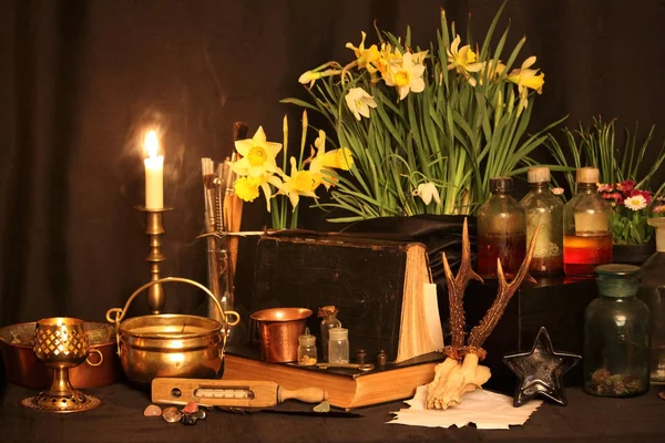 Black Magic Spells. Wiccan spells and herbs. Still Live: Old oil lamps, antique books, dried rose buds, a burning candle in a copper bowl, medicine bottles, lavender, Pulsatilla pratensis on an antique background. Wicca background.