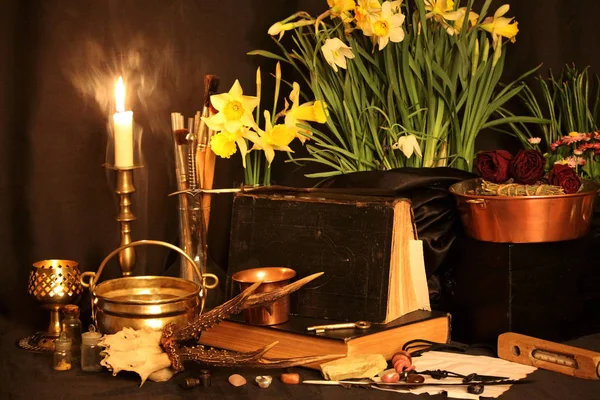 Black Magic Spells. Wiccan spells and herbs. Still Live: Old oil lamps, antique books, dried rose buds, a burning candle in a copper bowl, medicine bottles, lavender, Pulsatilla pratensis on an antique background. Wicca background.