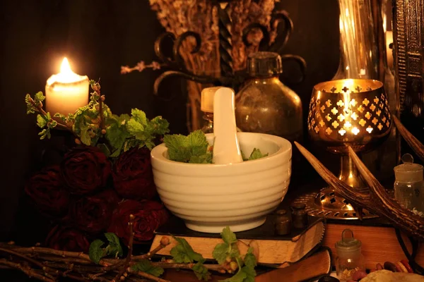 Kara büyü büyü. Wiccan büyüler ve otlar. Hala canlı: Eski yağ lambaları, antika kitap, bakır kase, ilaç şişeleri, lavanta, Pulsatilla pratensis bir antika arka plan üzerinde yanan bir muma gül tomurcukları kurutulmuş. Wicca arka plan.