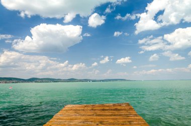 Beyaz kabarık bulutların altında yazın gökyüzü arka planında, denizde ahşap iskele. 