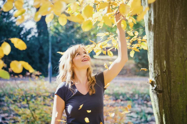 在城市公园里 金发美女和黄色的秋叶玩耍 — 图库照片