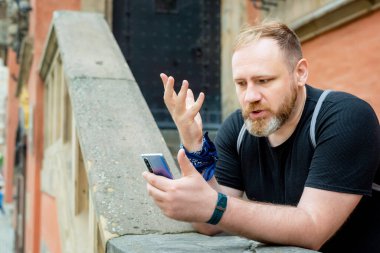 Yetişkin bir adam şehir merkezinde akıllı telefonla konuşur. Adamın akıllı telefondan bir video görüşmesi var.