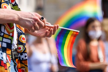 İnsan eli LGBT kağıt bayrağını tutuyor. Önplanda LGBT gökkuşağı bayrağı bulanık arkaplanlı eşitlik haklarının bir sembolü olarak. Tüm insanlar için eşitlik hakları