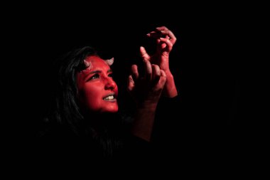 Cadılar Bayramı konsepti Kırmızı makyajlı ve küçük boynuzlu şeytan kadının vesikalığı, siyah elbiseler giyiyor, duygusal ifadeli, siyah arka planda fotokopi alanı ile poz veriyor..