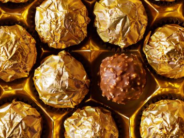 Üstten altın folyo görünümlü çikolata topları, açık kaplama folyoda bir pralin.