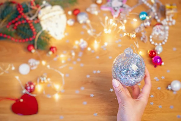 クリスマスのコンセプト 人間の手は 背景にお祝いの光とクリスマスの装飾が施されたガラスのクリスマスボールを保持します — ストック写真