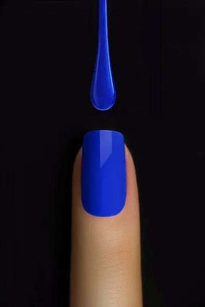 Drop of blue nail polish dripping on nail isolated on black. Finger point isolated white background.