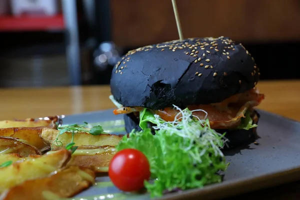 Black burger with meat patty, cheese, tomatoes, mayonnaise, fren