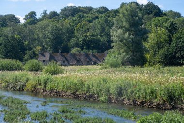Bibury Gloucestershire 'daki Arlington Row Kulübeleri önlerinde dere ve çayır olan Cotswold' lar.