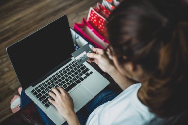 Kredi kartı basılı tutup dizüstü bilgisayar ve akıllı telefon kullanan genç kadın. Online alışveriş kavramı, teknoloji ve internet kavramı.