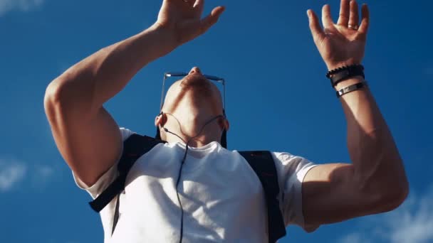 Joven bailando con auriculares en el fondo del cielo — Vídeo de stock