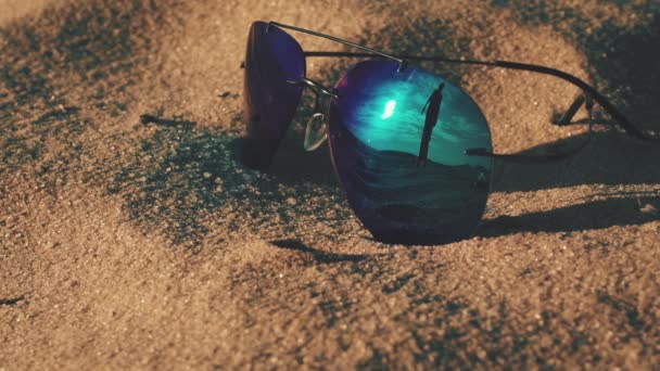 Gafas de sol tumbadas en la playa y silueta de niña reflectante — Vídeos de Stock