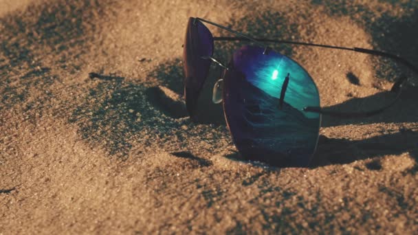 Okulary przeciwsłoneczne leżące na plaży i odzwierciedlające sylwetkę dziewczyny — Wideo stockowe