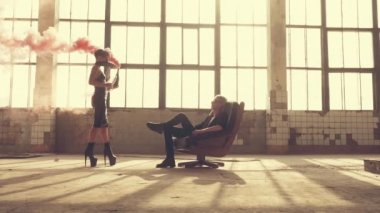 Kırmızı bir şişe dumanla maskeli kadın ve koltukta erkek