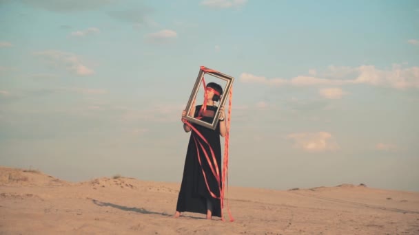 Vrouw geblinddoekt met fotolijstje in de woestijn — Stockvideo