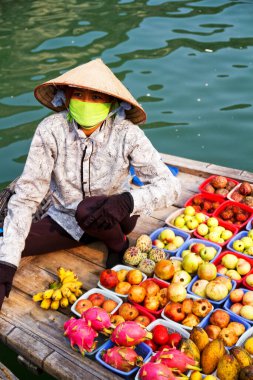 HA LONG BAY, VİETNAM - Eylül 01: Kimliği belirsiz kadın, 1 Eylül 2012 'de Ha Long Körfezi, Vietnam' da teknesinden meyve satmaktadır. Süzülen piyasalar çok popülerdir çünkü hareket etmenin tek yolu budur..