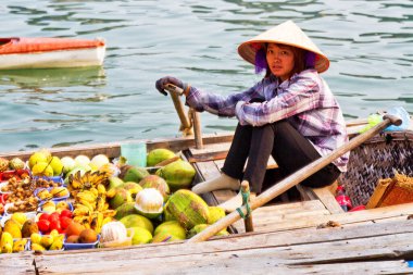 HA LONG BAY, VİETNAM - Eylül 01: Kimliği belirsiz kadın, 1 Eylül 2012 'de Ha Long Körfezi, Vietnam' da teknesinden meyve satmaktadır. Süzülen piyasalar çok popülerdir çünkü hareket etmenin tek yolu budur..