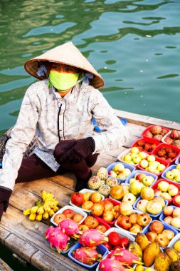 HA LONG BAY, VİETNAM - Eylül 01: Kimliği belirsiz kadın, 1 Eylül 2012 'de Ha Long Körfezi, Vietnam' da teknesinden meyve satmaktadır. Süzülen piyasalar çok popülerdir çünkü hareket etmenin tek yolu budur..