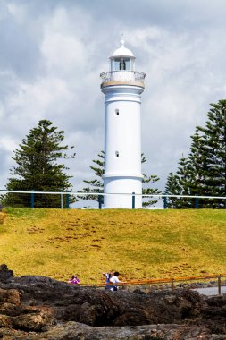 Deniz feneri sembolik olarak mavi gökyüzünün altındaki yeşil çimlerin üzerinde duruyor. Kiama, Yeni Güney Galler, Avustralya.