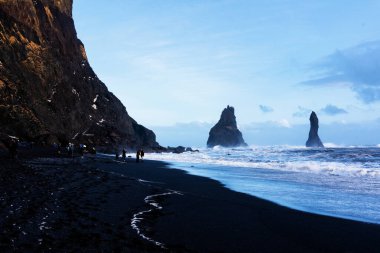 Reynisfjara 'nın kara kumsalı ve İzlanda' nın güney kıyısındaki Dyrholaey 'den Reynisfjall Dağı..