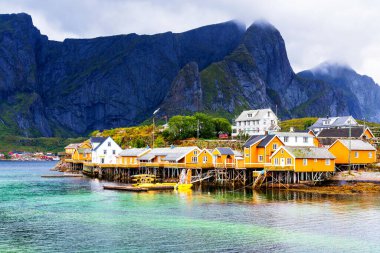 Norveç 'in Lofoten Adaları' ndaki kırmızı ve sarı rorbu evleriyle ünlü bir turistik bölge olan Hamnoy balıkçı köyü. Sakin, bulanık su