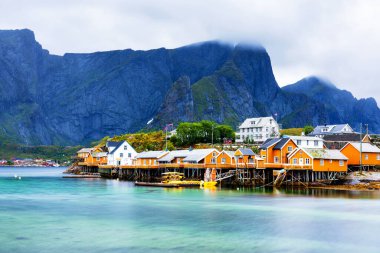 Norveç 'in Lofoten Adaları' ndaki kırmızı ve sarı rorbu evleriyle ünlü bir turistik bölge olan Hamnoy balıkçı köyü. Sakin, bulanık su