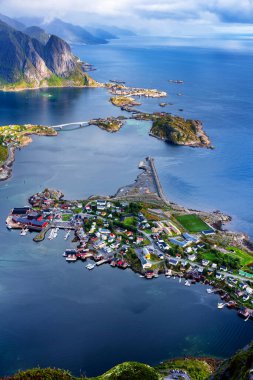 Göz kamaştırıcı dağların güneşli panoramik manzarası ve Reinebringen tepesinden Norveç 'in Lofoten adalarındaki Reine köyü. Gökkuşağı ve engebeli tepeleri olan manzaralı bir manzara.