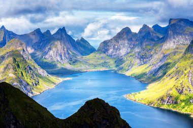 Göz kamaştırıcı dağların güneşli panoramik manzarası ve Reinebringen tepesinden Norveç 'in Lofoten adalarındaki Reine köyü. Gökkuşağı ve engebeli tepeleri olan manzaralı bir manzara.