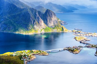 Göz kamaştırıcı dağların güneşli panoramik manzarası ve Reinebringen tepesinden Norveç 'in Lofoten adalarındaki Reine köyü. Gökkuşağı ve engebeli tepeleri olan manzaralı bir manzara.