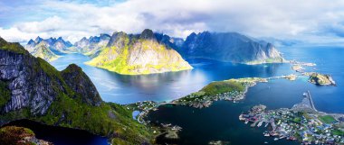 Göz kamaştırıcı dağların güneşli panoramik manzarası ve Reinebringen tepesinden Norveç 'in Lofoten adalarındaki Reine köyü. Gökkuşağı ve engebeli tepeleri olan manzaralı bir manzara.