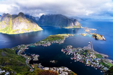 Göz kamaştırıcı dağların güneşli panoramik manzarası ve Reinebringen tepesinden Norveç 'in Lofoten adalarındaki Reine köyü. Gökkuşağı ve engebeli tepeleri olan manzaralı bir manzara.