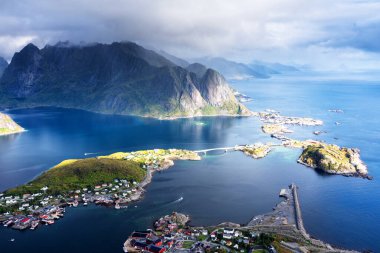 Göz kamaştırıcı dağların güneşli panoramik manzarası ve Reinebringen tepesinden Norveç 'in Lofoten adalarındaki Reine köyü. Gökkuşağı ve engebeli tepeleri olan manzaralı bir manzara.