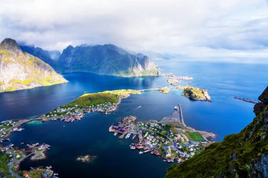 Göz kamaştırıcı dağların güneşli panoramik manzarası ve Reinebringen tepesinden Norveç 'in Lofoten adalarındaki Reine köyü. Gökkuşağı ve engebeli tepeleri olan manzaralı bir manzara.