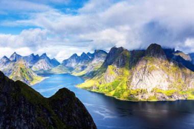Göz kamaştırıcı dağların güneşli panoramik manzarası ve Reinebringen tepesinden Norveç 'in Lofoten adalarındaki Reine köyü. Gökkuşağı ve engebeli tepeleri olan manzaralı bir manzara.