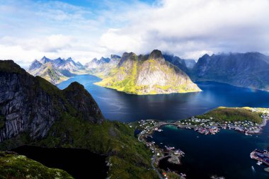 Göz kamaştırıcı dağların güneşli panoramik manzarası ve Reinebringen tepesinden Norveç 'in Lofoten adalarındaki Reine köyü. Gökkuşağı ve engebeli tepeleri olan manzaralı bir manzara.