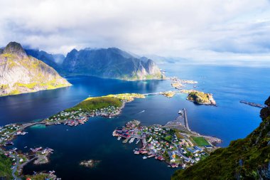 Göz kamaştırıcı dağların güneşli panoramik manzarası ve Reinebringen tepesinden Norveç 'in Lofoten adalarındaki Reine köyü. Gökkuşağı ve engebeli tepeleri olan manzaralı bir manzara.