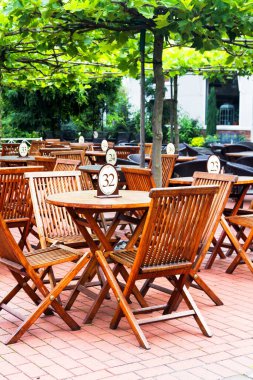 Kafede ya da restoranda tuğla verandada bir sürü ahşap meşe masa ve sandalye var.